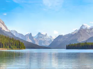 Maligne Lake in Jasper national park, Alberta, Canada taken on a sunny day with the lake in the foreground, trees and mountains in the distance.