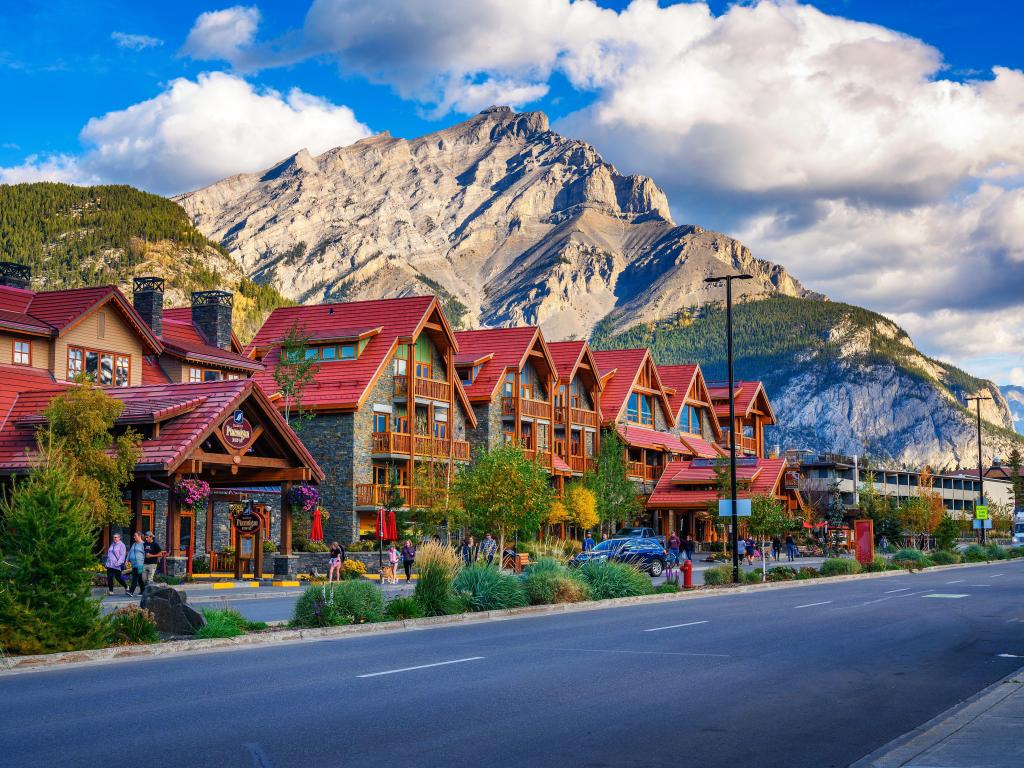 Banff, Alberta, Canada with a scenic street view of the Banff Avenue with cars and tourists and the famous mountains in the distance on a sunny day. 