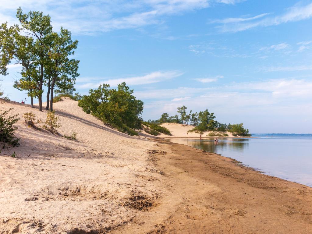 Sandbanks Provincial Park, Prince Edward County, Ontario with a beautiful sandy beach, dotted with trees, calm water and taken on a sunny day.