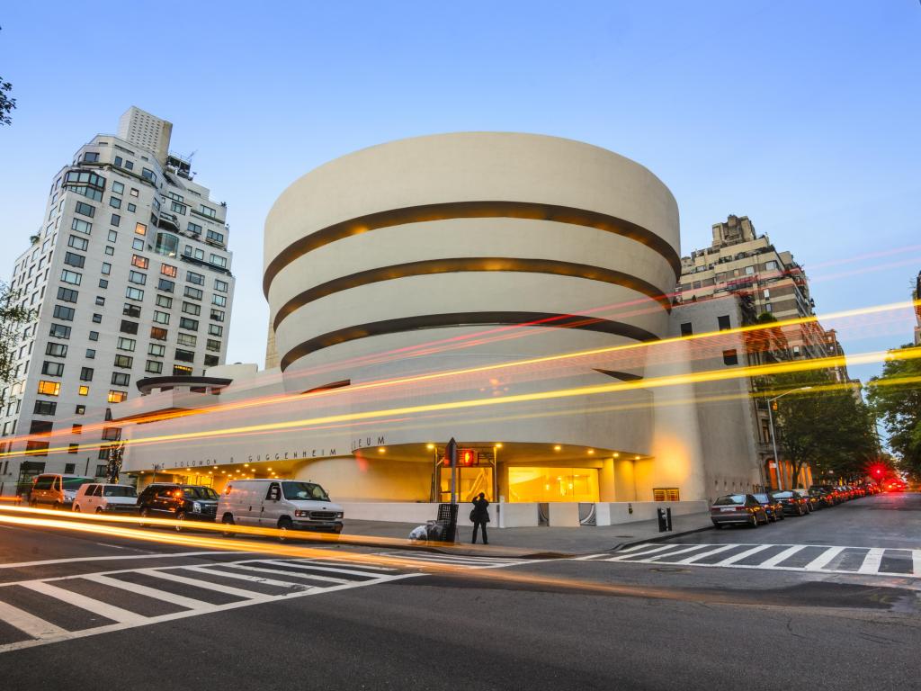 White, circular exterior of the museum during sunset, with long exposure lights of cars in the foreground