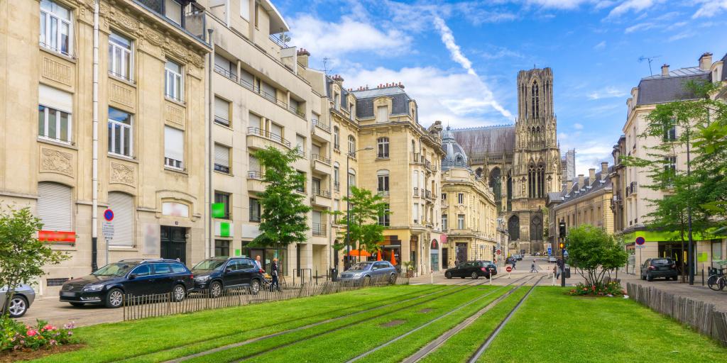 A street in Reims, France, with big stone buildings to the right and tram tracks surrounded by grass