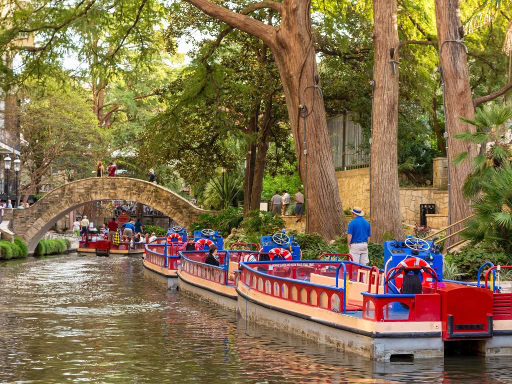 Blue, red and white colored river boats on San Antonio River, docked by the famous San Antonio River Walk