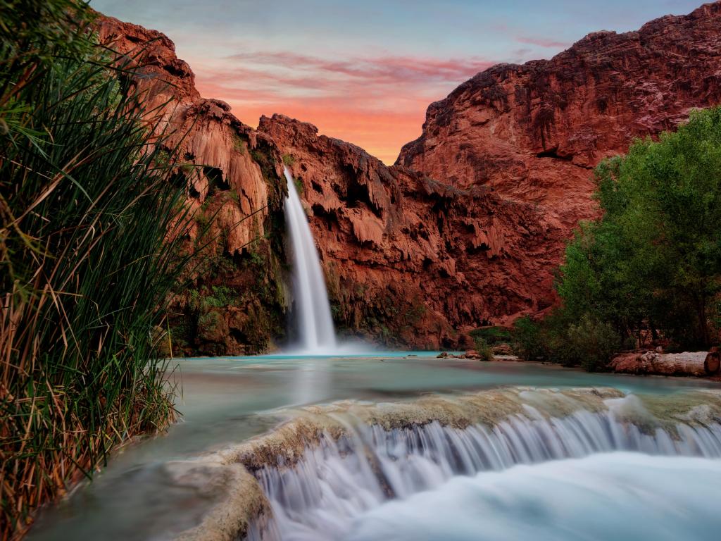 Havasu Falls, Grand Canyon, Arizona, USA taken at sunset with a river in the foreground and the waterfall against the red rock in the background. 