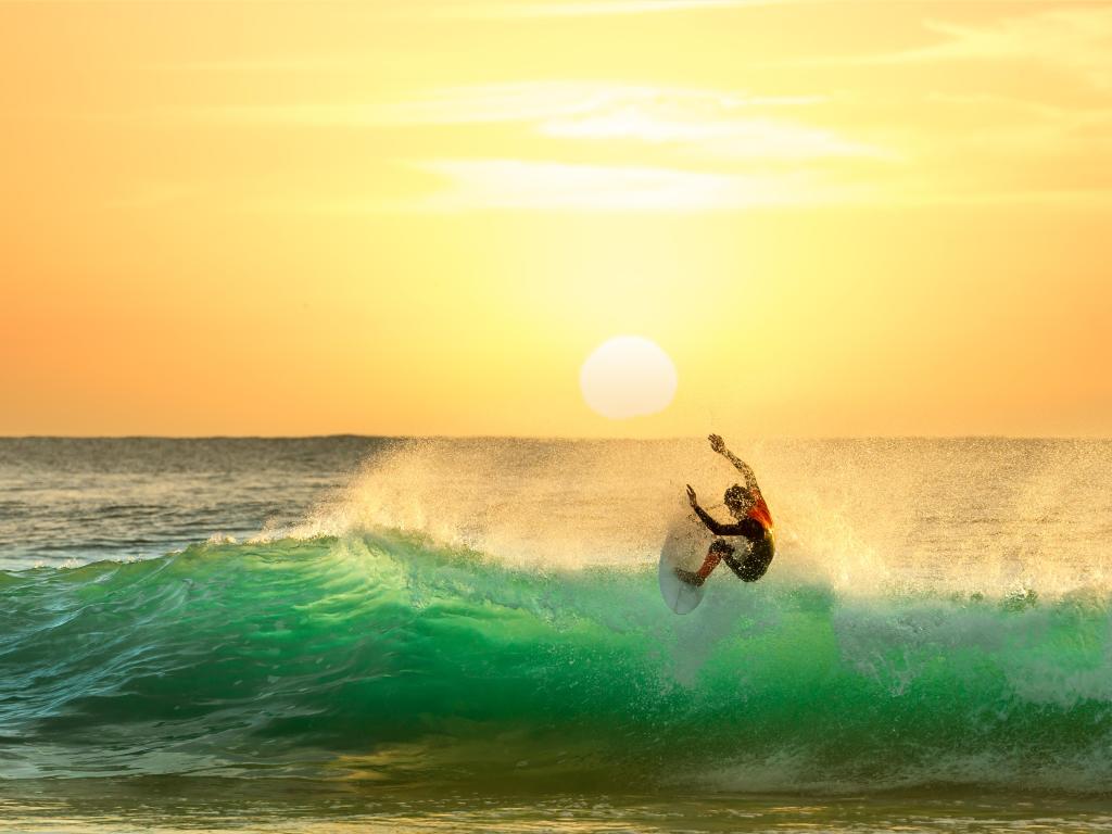 Surfer riding a wave with the setting sun illuminating the water