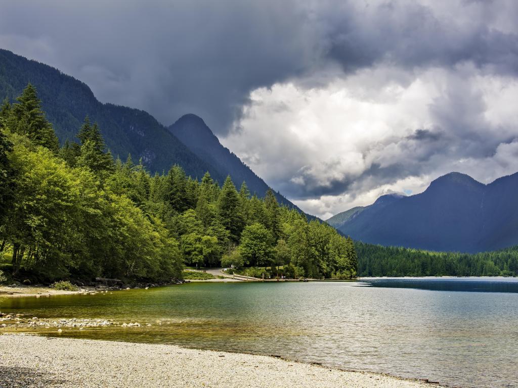Golden Ears Provincial Park, British Columbia, Canada taken at Alouette Lake with a dramatic sky in the background, the shore in the foreground and trees between the two.