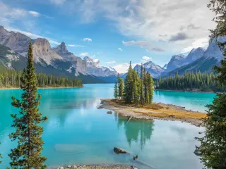 Beautiful blue lake surrounded by evergreen trees with rugged mountains in the background on a blue but cloudy day