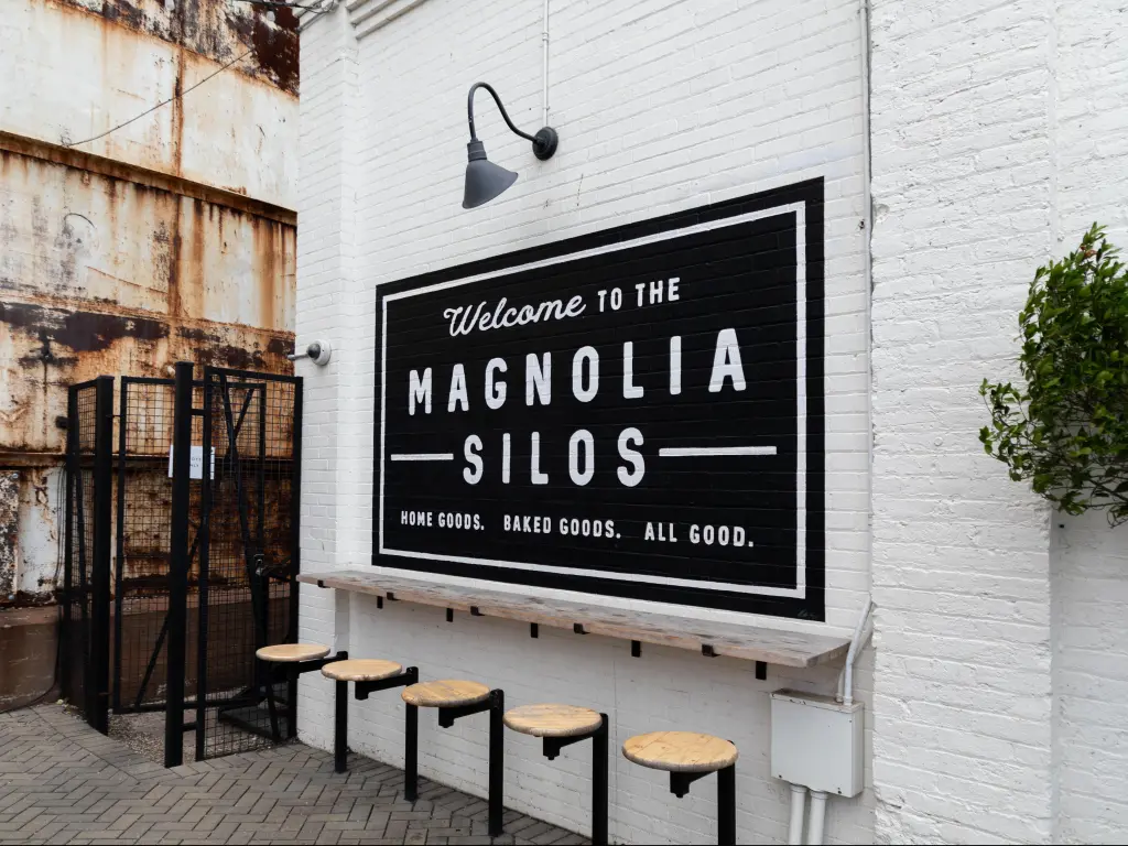 A black and white sign on the wall of Magnolia Silos in Waco Texas, with whitewashed bricks behind