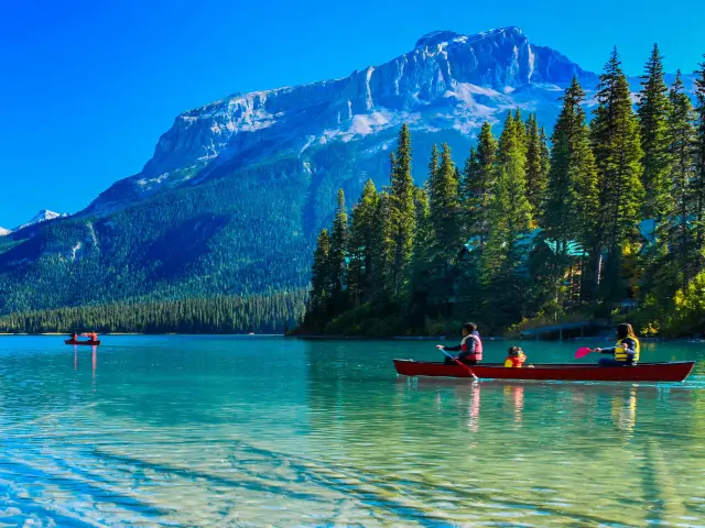 People canoeing on the clear and stunning Emerald Lake with mountains and forests in the background