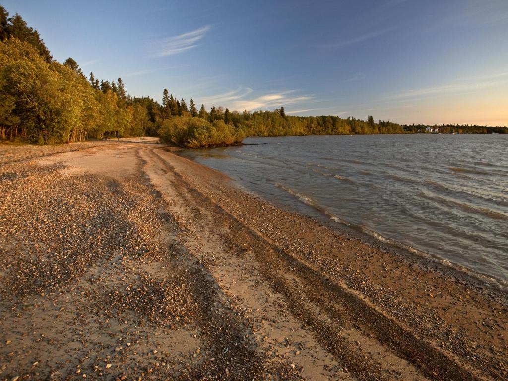 Lake Winnipeg, Manitoba, Canada taken at sunrise with the shore and water in the foreground and trees in the background.