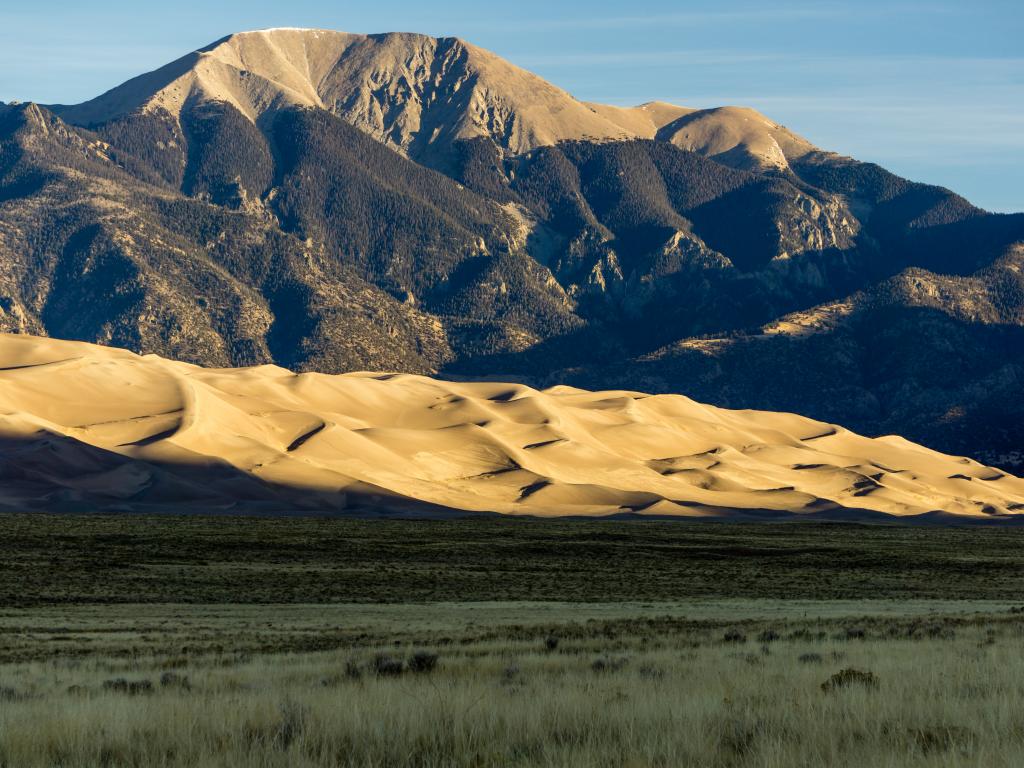 An image of a portion of the Great Sand Dunes National Park being hit by early morning sunlight. Mountains are also in sight.