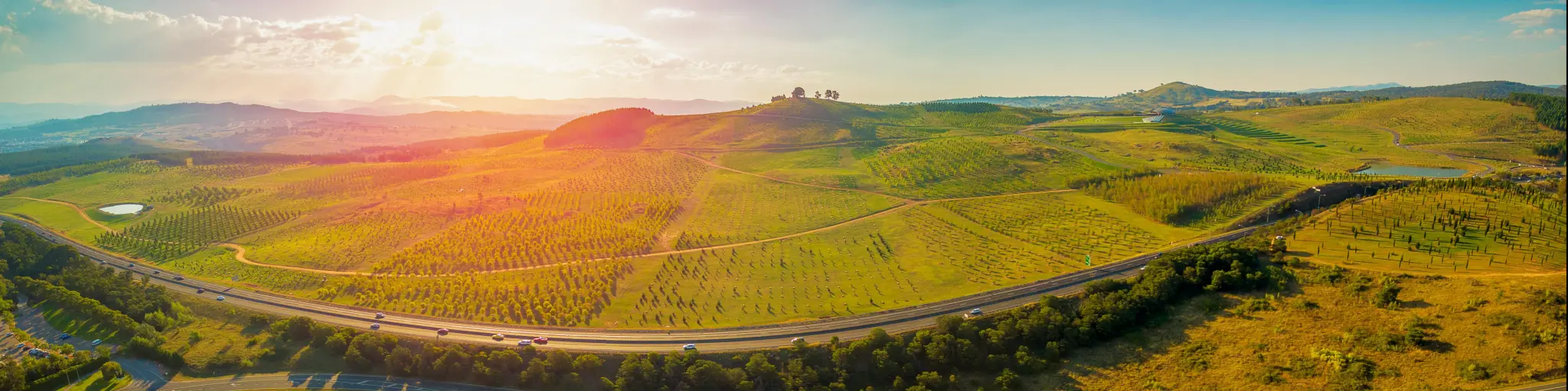 Aerial panorama of green fields and gently rolling hills - Tuggeranong Parkway and National Arboretum at sunset in Canberra, Australia