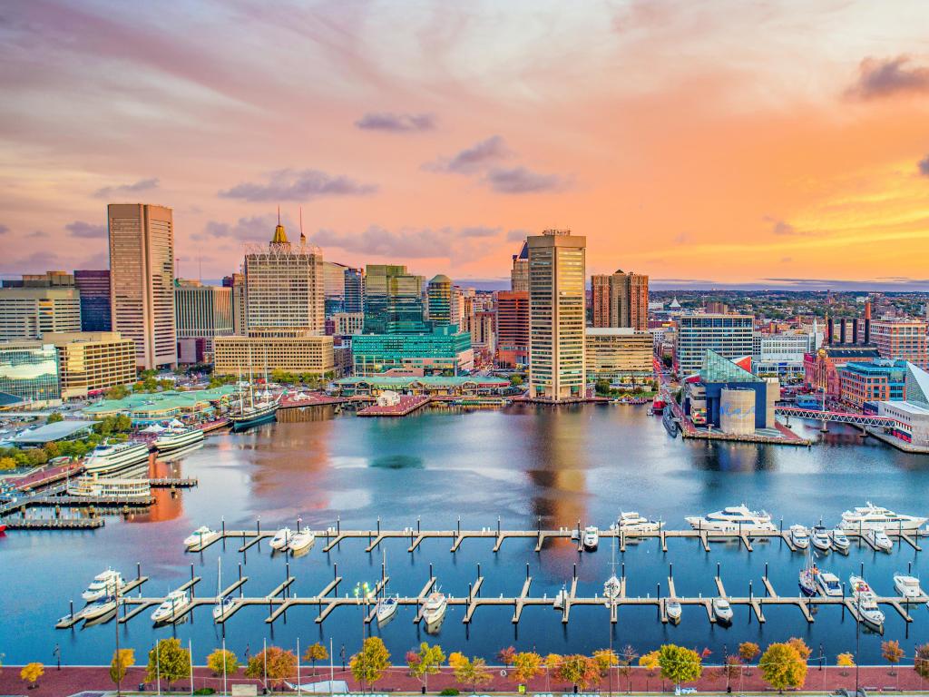 Baltimore, Maryland, USA taken at the Inner Harbor at sunset with a colorful sky and city skyline in the distance. 