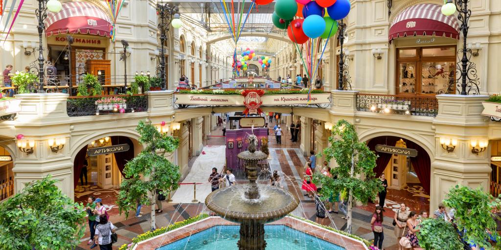 Inside the GUM (main department store) at the Red Square, Russia, with a fountain in the middle, some greenery and ornate arches 