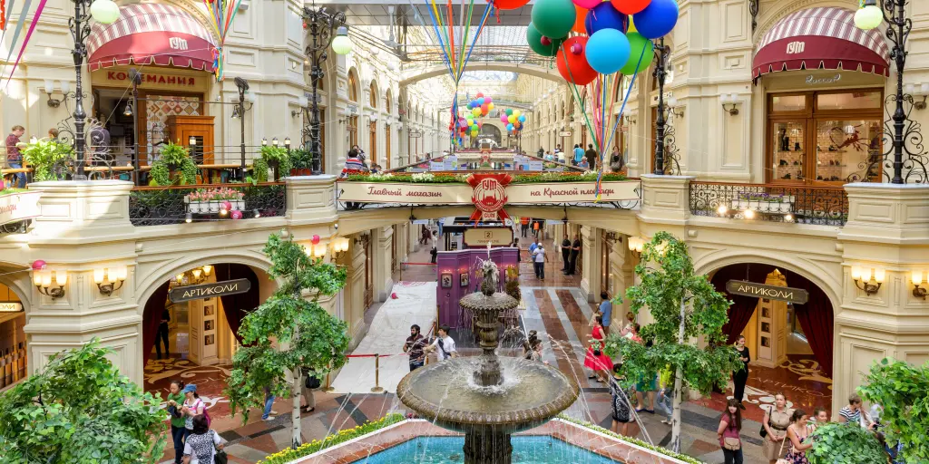 Inside the GUM (main department store) at the Red Square, Russia, with a fountain in the middle, some greenery and ornate arches 