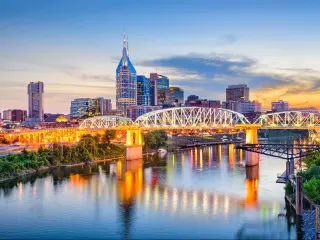Nashville, Tennessee, USA downtown skyline on the Cumberland River at dusk with the bridge lit up and reflecting in the water below. 