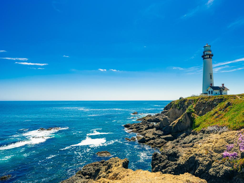 Pigeon Point Lighthouse at Big Sur, surrounded with colourful wildflowers in spring time, the ocean and a blue sky.