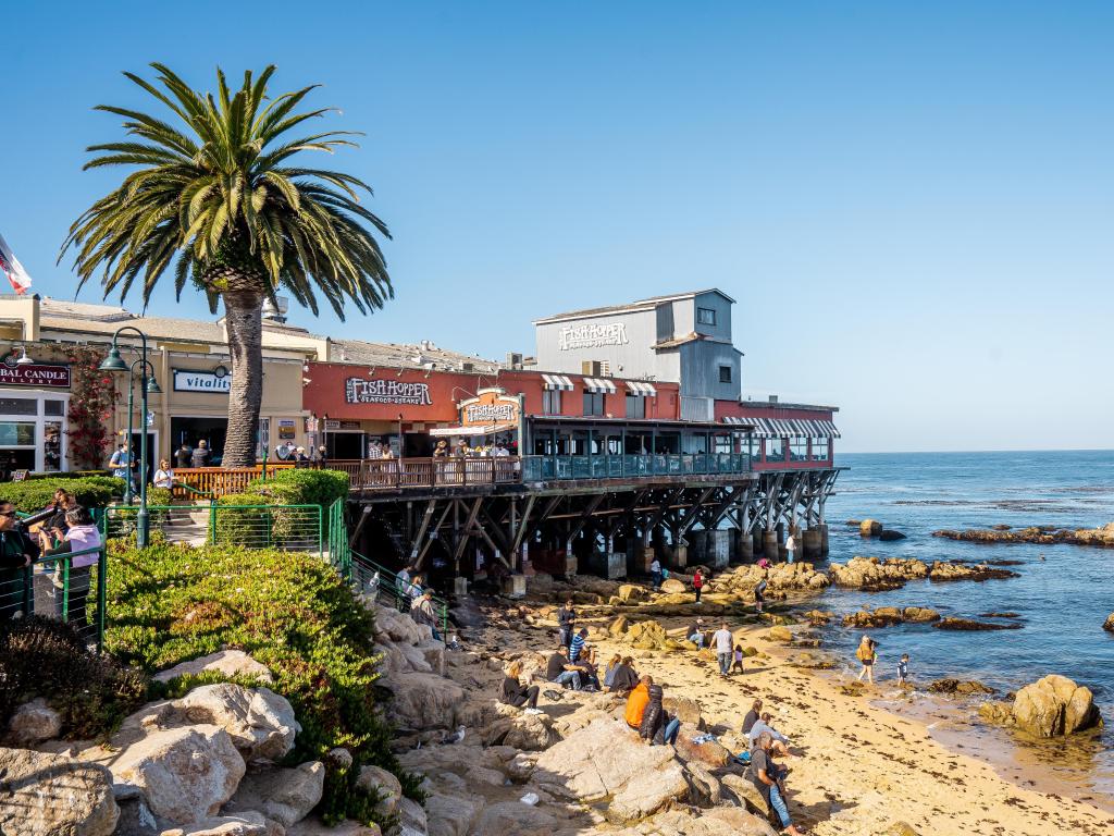 View of historic 700 Cannery Row Mall along boardwalk at Monterey Bay, with blue skies and ocean in the background