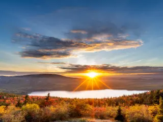 Acadia National Park, USA taken at sunset with fall colored trees in the foreground, the lake and hills in the distance with a dramatic and stunning sky.