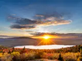 Acadia National Park, USA taken at sunset with fall colored trees in the foreground, the lake and hills in the distance with a dramatic and stunning sky.