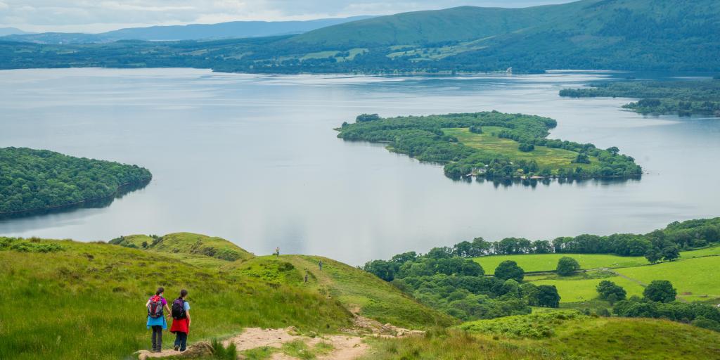 Two hikers walk on a hill overlooking Loch Lomond in Scotland