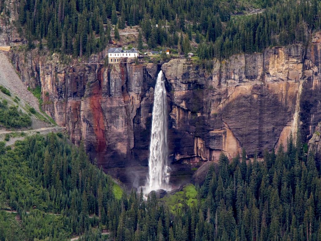 The tallest free-flowing waterfall in Colorado cascades down a sheer rock face with pine trees on surrounding slopes