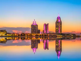 Mobile, Alabama, USA with a large expanse of water in the foreground and the downtown skyline in the distance reflecting in the water at dusk.