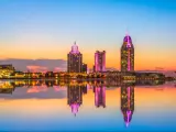Mobile, Alabama, USA with a large expanse of water in the foreground and the downtown skyline in the distance reflecting in the water at dusk.