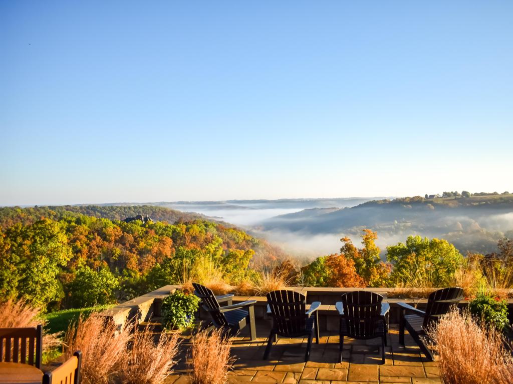 A patio overlooks an Ozarks valley with fall foliage and fog as the morning sun rises.