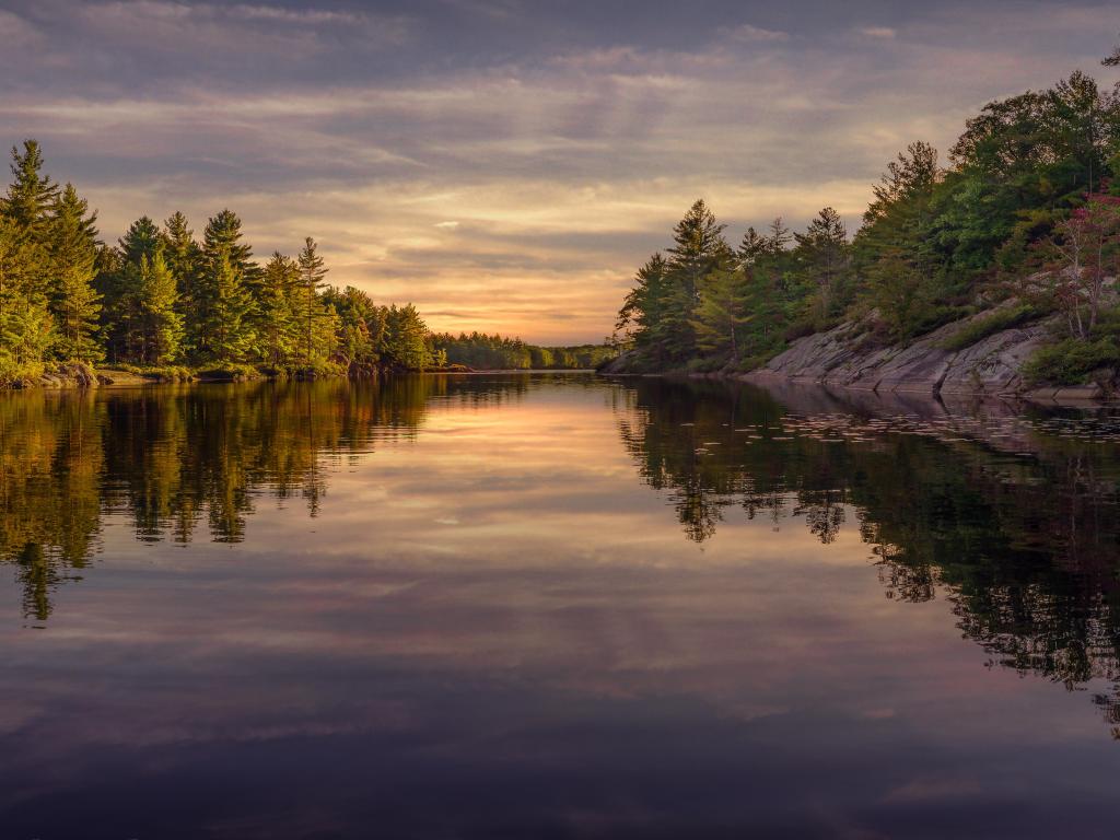 Rocky shores with trees reflected onto glass-like water with blue sunset light