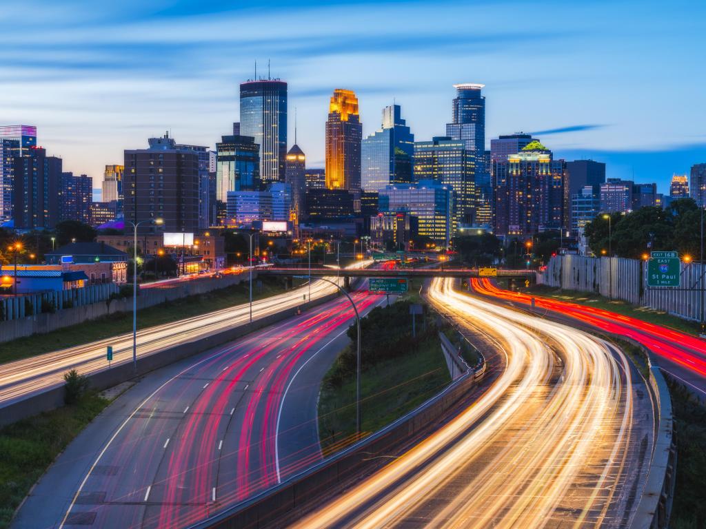 Minneapolis, USA with the city skyline in the distance and traffic lights at night in the foreground creating a bright light on the road. 