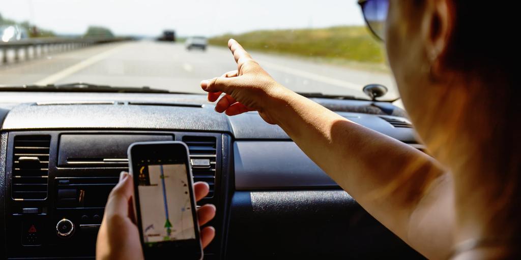Person using navigation app on phone and pointing out of window towards a road