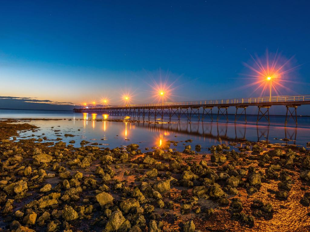 Rocky beach with wooden pier projecting out over the water with bright lights reflected