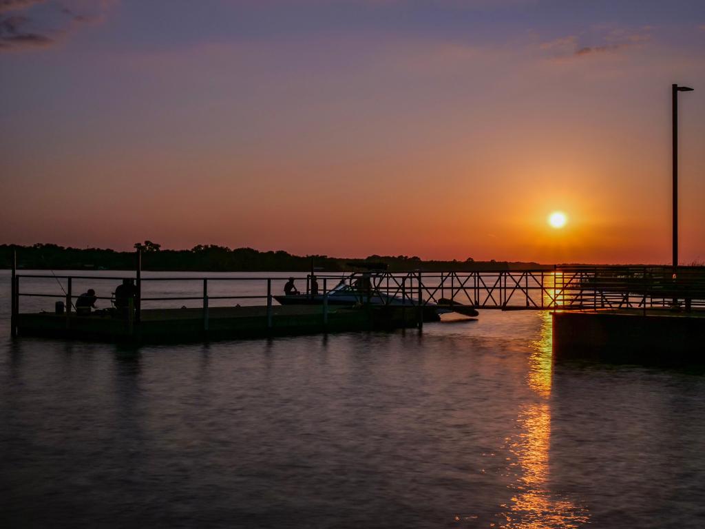 Sunset over Lake Worth, Texas, with silhouette of boats and a jetty in the foreground 