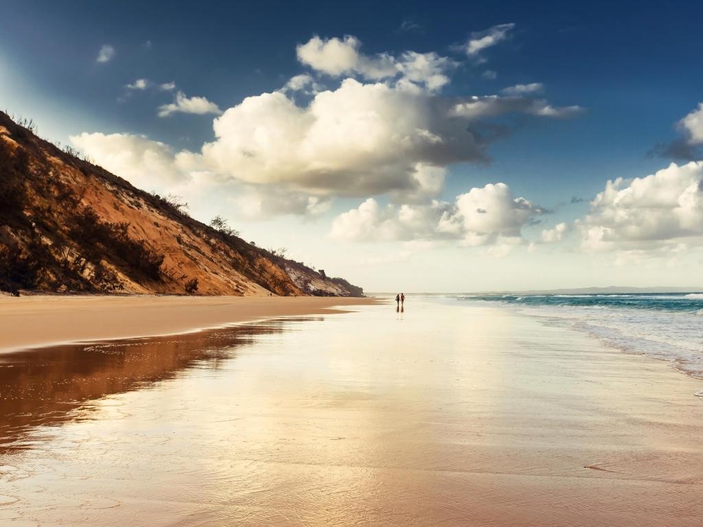 Rainbow Beach, Queensland, Australia at sunset with a couple walking into the distance on a long beach, cliffs to one side and the sea to the other.