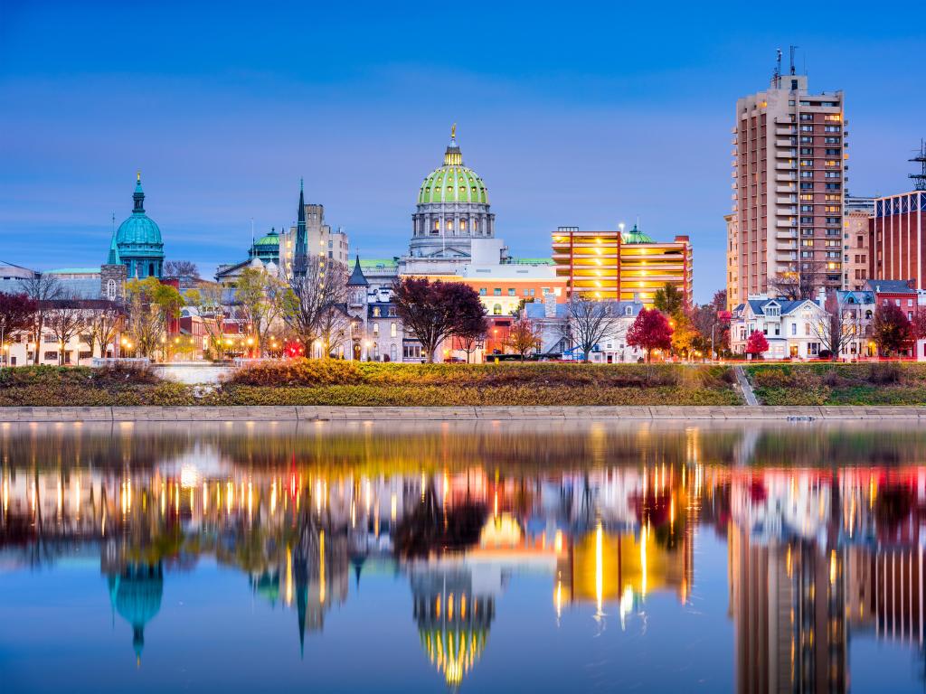 Harrisburg, Pennsylvania, USA with the city skyline in the background and the Susquehanna River in the foreground, taken after sunset with the city lights reflecting in the water.