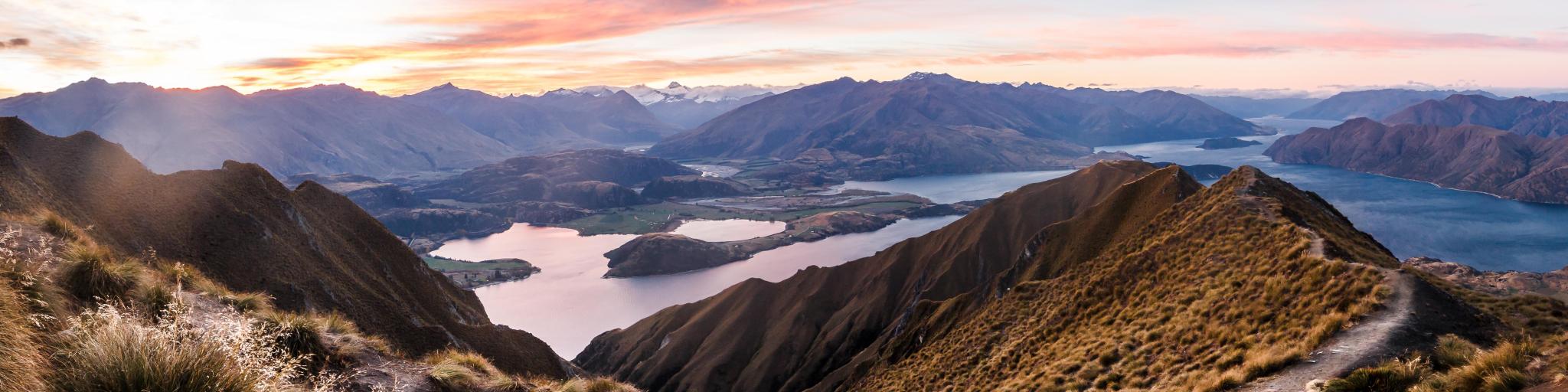 Queenstown, New Zealand with a panorama at sunset of Roys Peak between Wanaka and Queenstown with a lake and mount aspiring and cook of the new zealand alps on the background