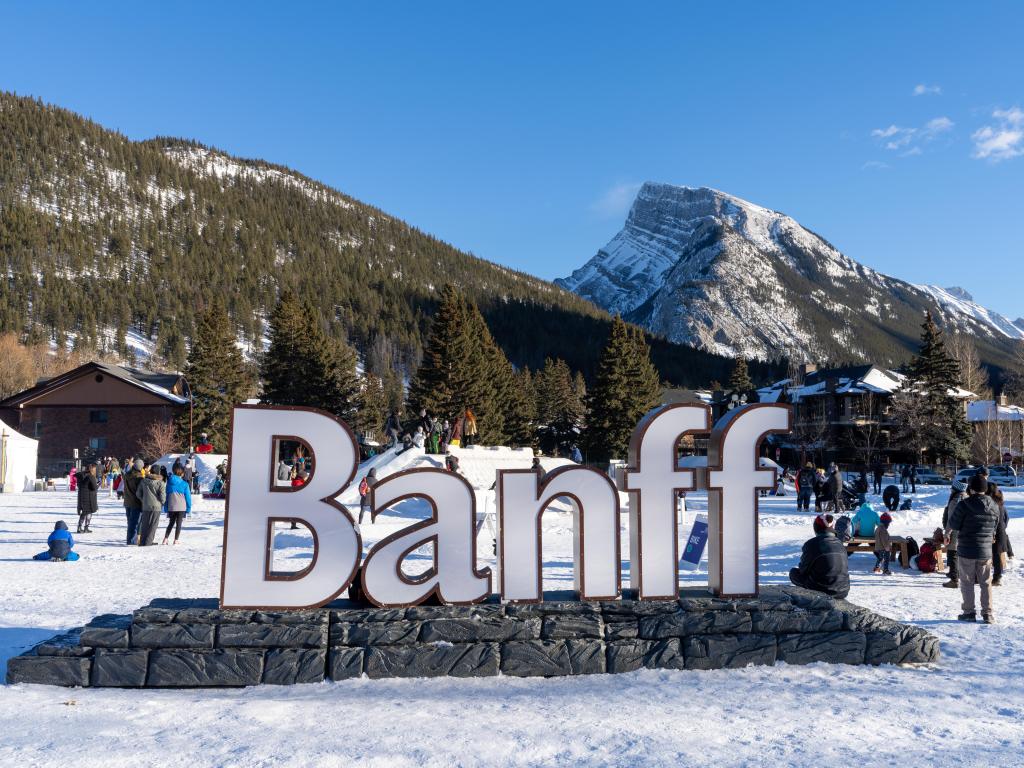 White "Banff" sign during winter with snow on the ground. Mountain view in the background on a sunny day