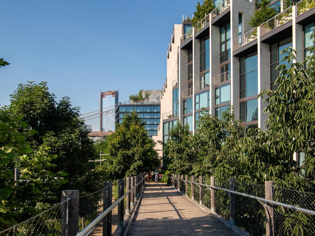View of 1 Hotel Brooklyn Bridge in daylight, with walkway along front and  tall trees dotted along the building