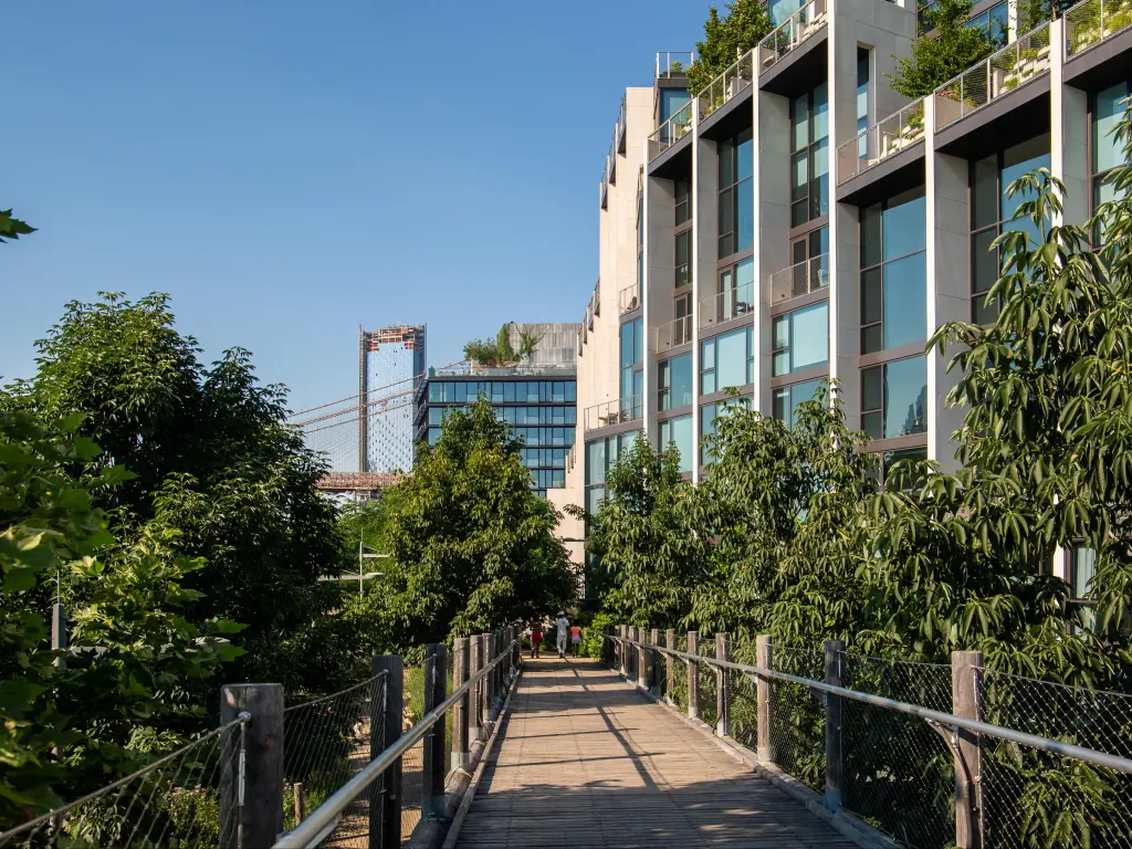 View of 1 Hotel Brooklyn Bridge in daylight, with walkway along front and  tall trees dotted along the building