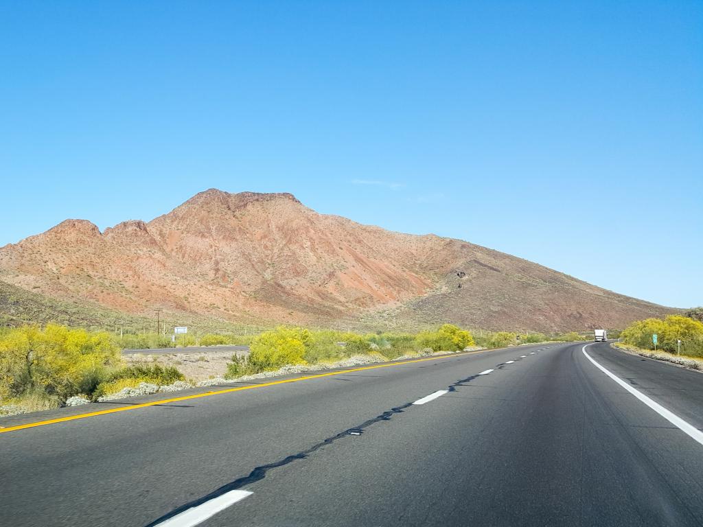 An empty highway of Interstate 10 with green bushes in the side along isolated hills and low rise mountain in Quartsize on a sunny weather