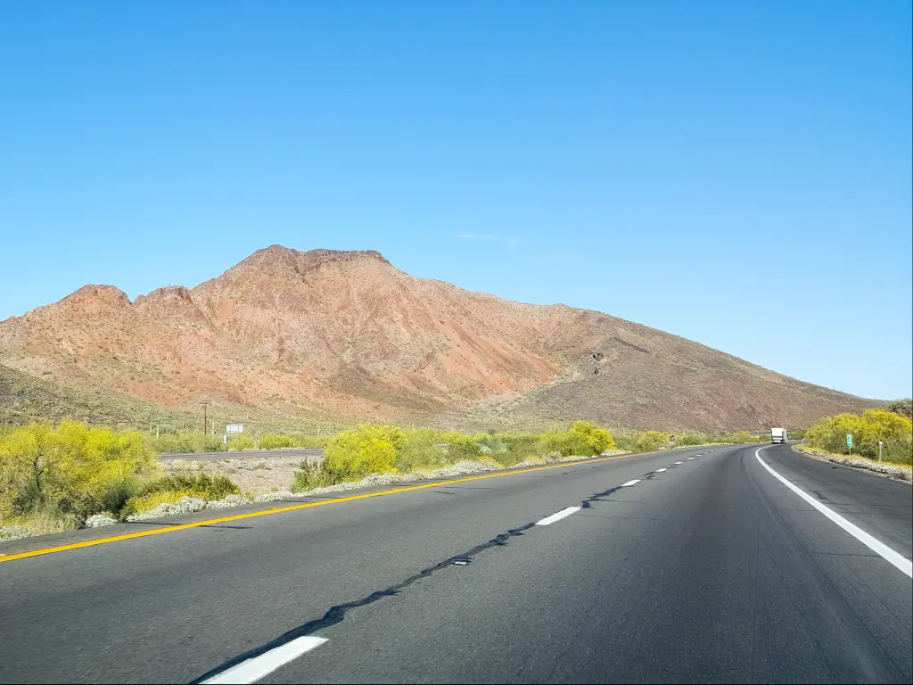 An empty highway of Interstate 10 with green bushes in the side along isolated hills and low rise mountain in Quartsize on a sunny weather