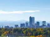 Panoramic view of high rise buildings of Denver skyline with green trees in the foreground and rocky mountains in the background