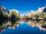 Yosemite National Park, USA on a sunny day with the lake reflecting mountains in the distance and trees lining the waters edge under a blue sky,