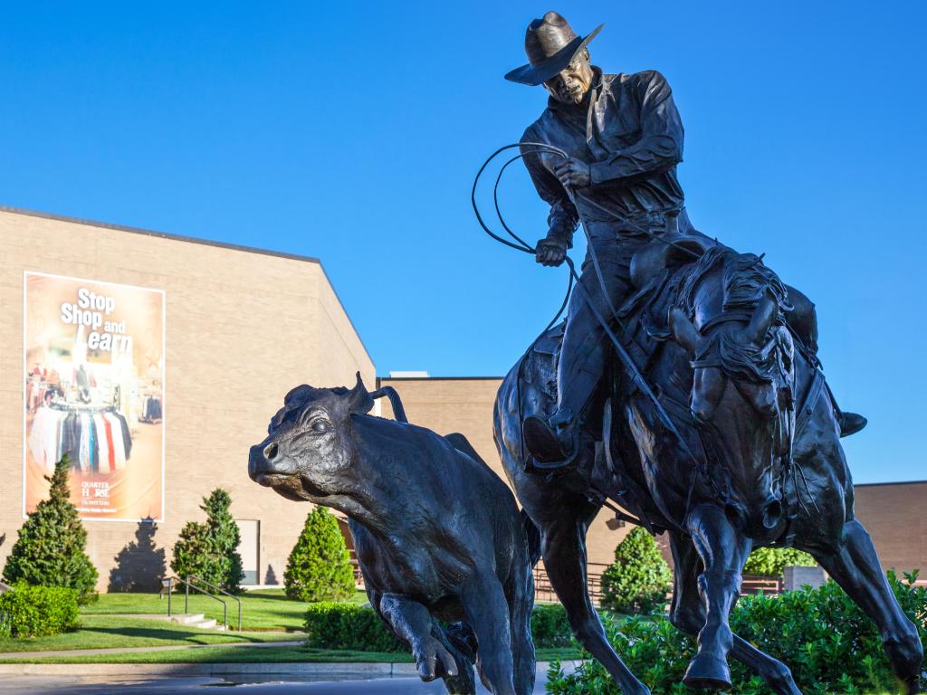 Bronze cowboy statue with a lasso, chasing after a cow while riding a horse