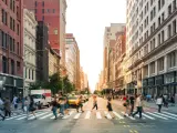 Pedestrians navigating a crosswalk at a busy intersection with the sun setting between the buildings