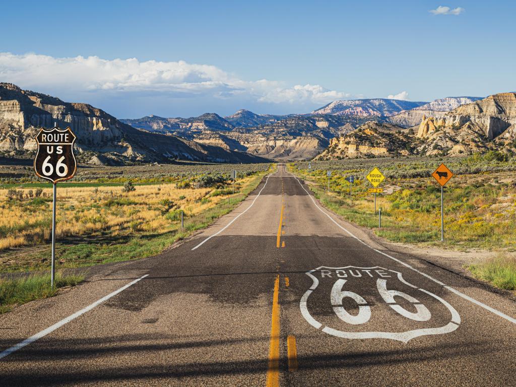 Long straight road labelled route 66 runs towards mountains in the distance