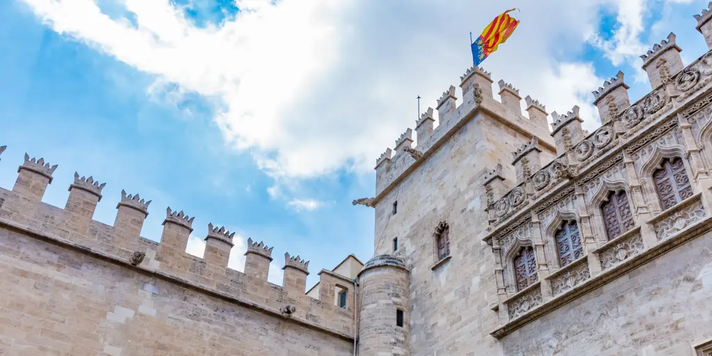 The stone building of Lonja de la Seda, in Valencia, Spain, with the battlements in view and a flag on top