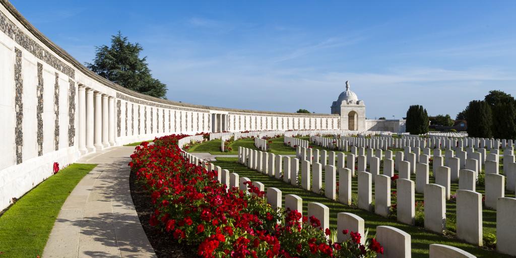 The curved wall of Tyne Cot cemetery, with rows of poppies and graves in front of it