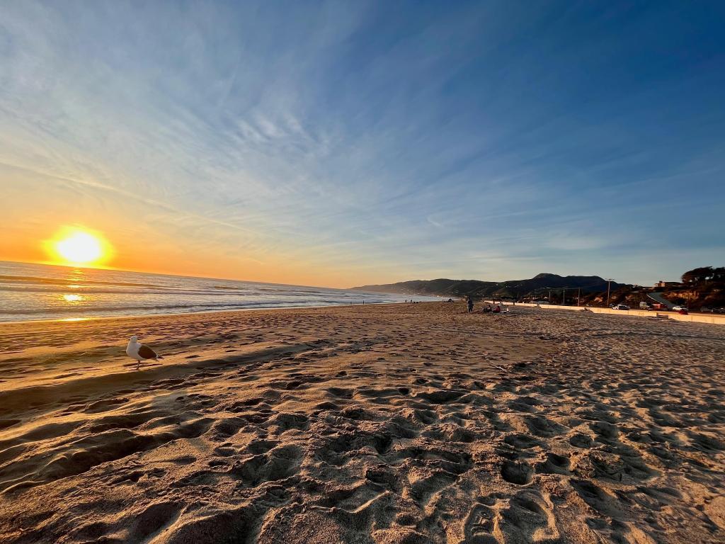 Beach sunset along the beach front of Zuma Beach, with sandy beach in the forefront 