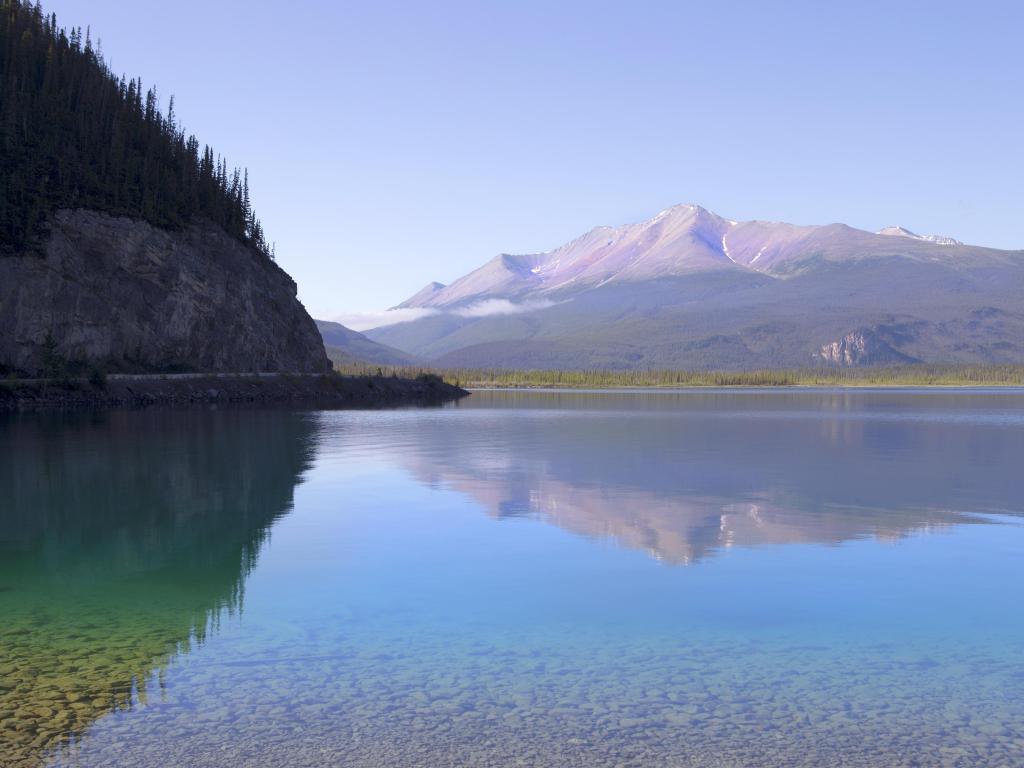 Muncho Lake in British Columbia, Canada with the calm water in the foreground and mountain in the distance taken on a sunny day.